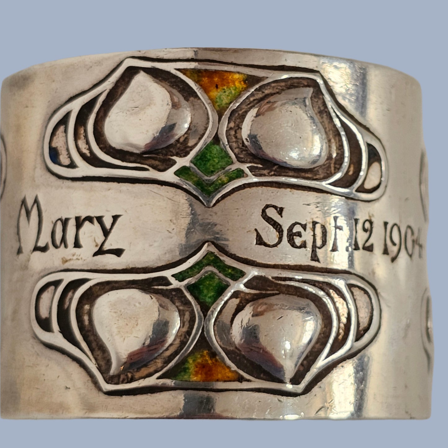 Silver and enamel Liberty & Co napkin ring with engraved design and text on a gray background