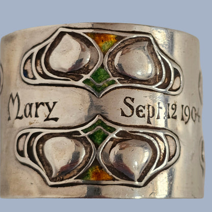 Silver and enamel Liberty & Co napkin ring with engraved design and text on a gray background